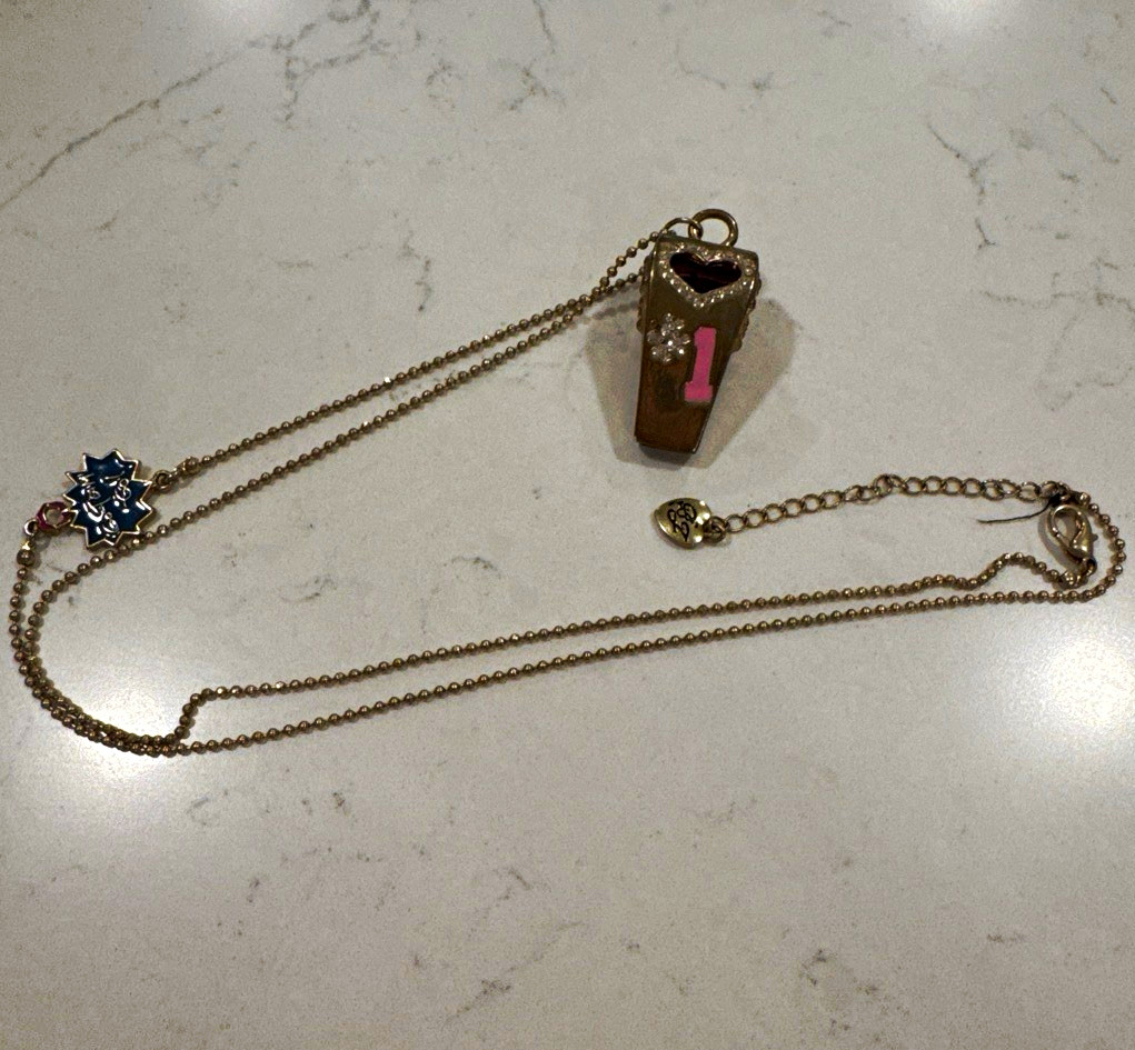 Gold-tone Betsy Johnson whistle necklace with rhinestones, a heart, and a charm.
