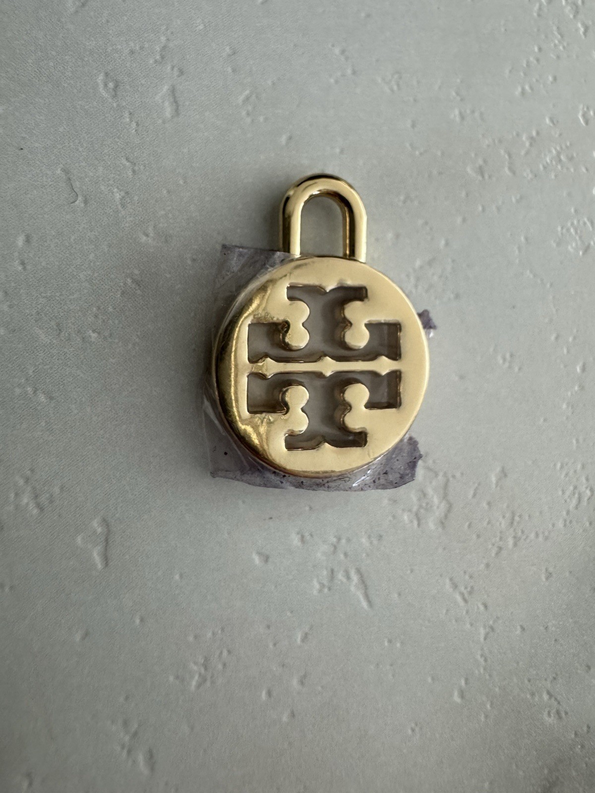 Tory Burch logo charm in gold tone Padlock-style loop for attaching to jewelry.