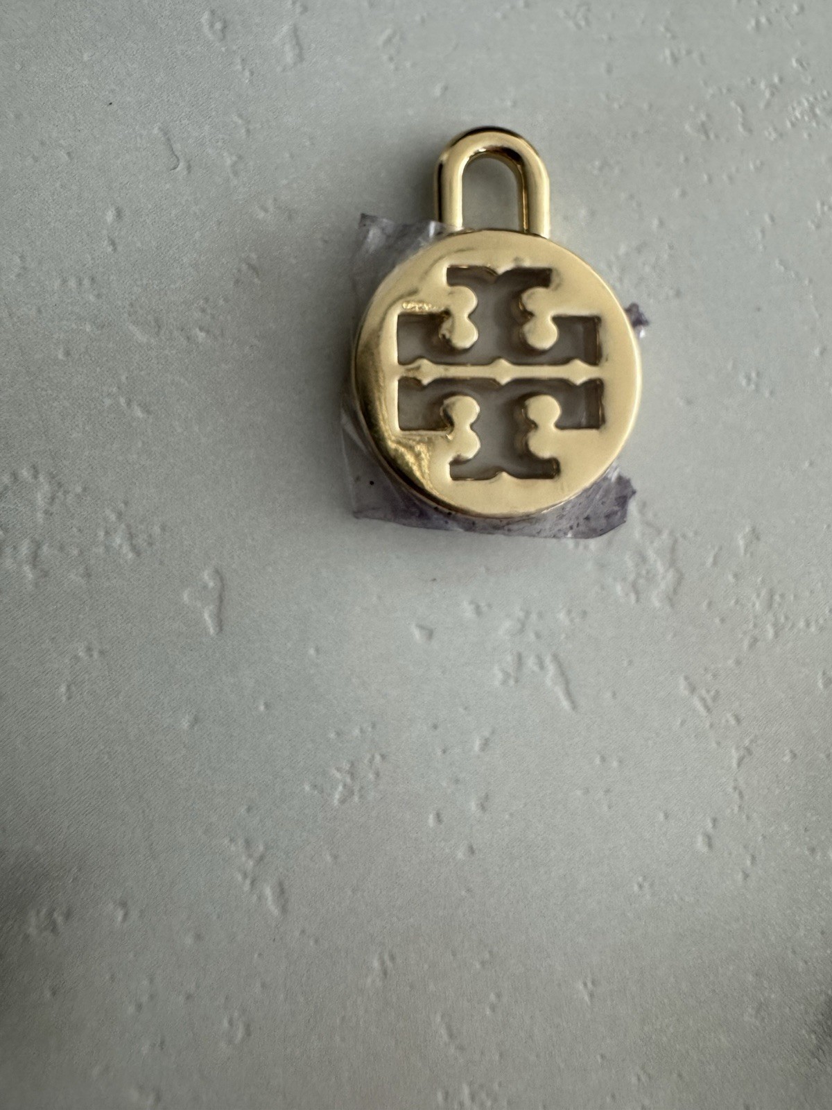 Tory Burch logo charm in gold tone Padlock-style loop for attaching to jewelry.