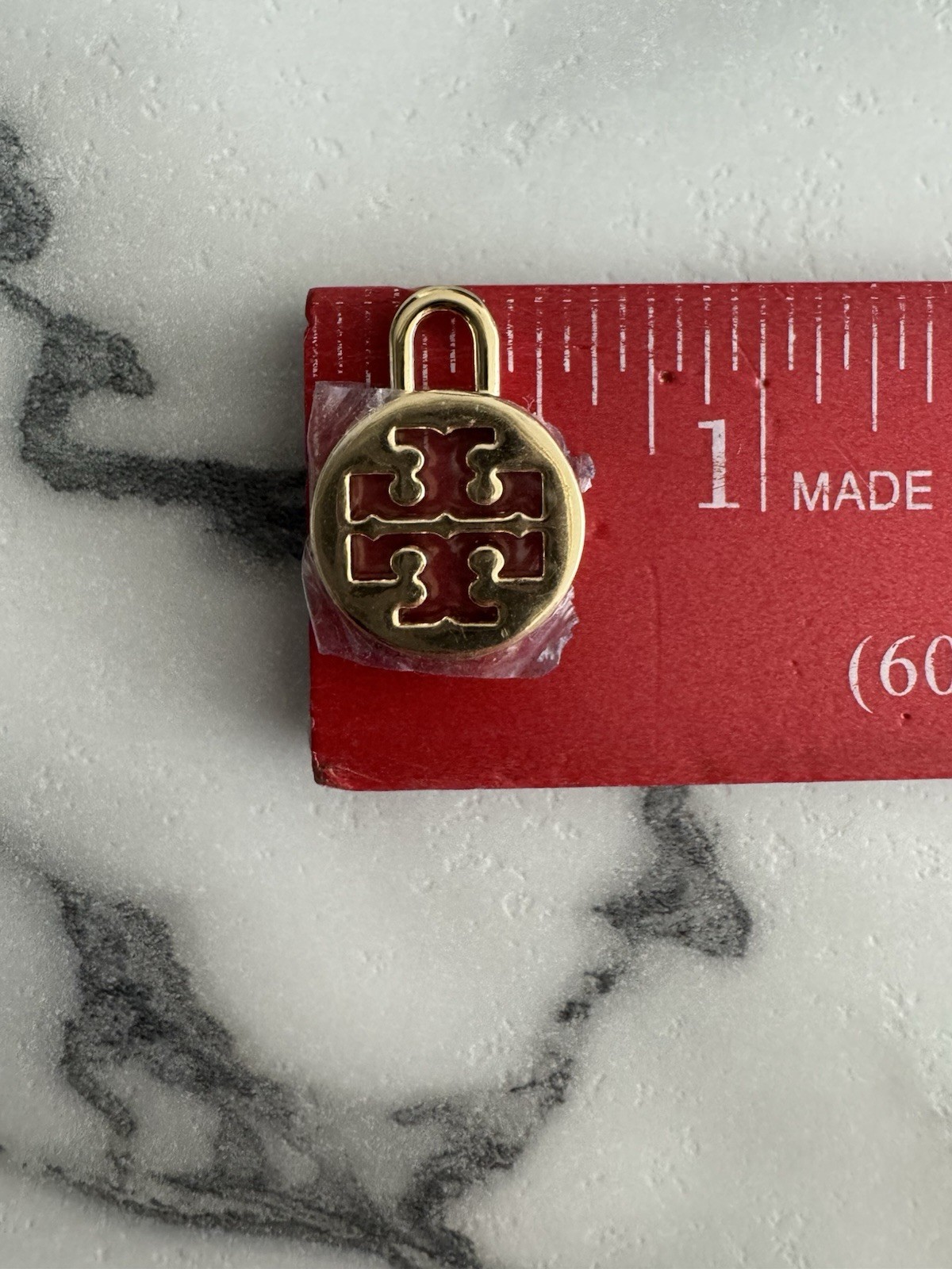 Tory Burch logo charm in gold tone Padlock-style loop for attaching to jewelry.